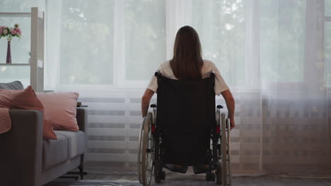 brunette woman moves wheelchair closer to bright window