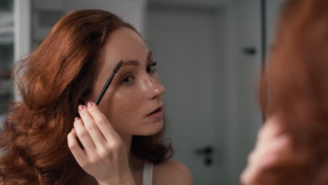 Caucasian-woman-brushing-eyebrows-in-the-mirror-reflection.