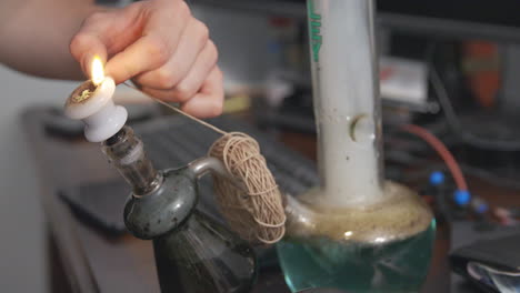 Hemp-wick-around-the-base-of-a-bong-is-lit-and-used-to-light-a-bowl-of-cannabis