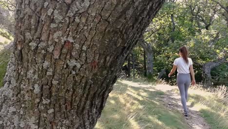 revealing shot of a young girl walking into a deep forest with old mossy trees in focus in front, pan right, slomo