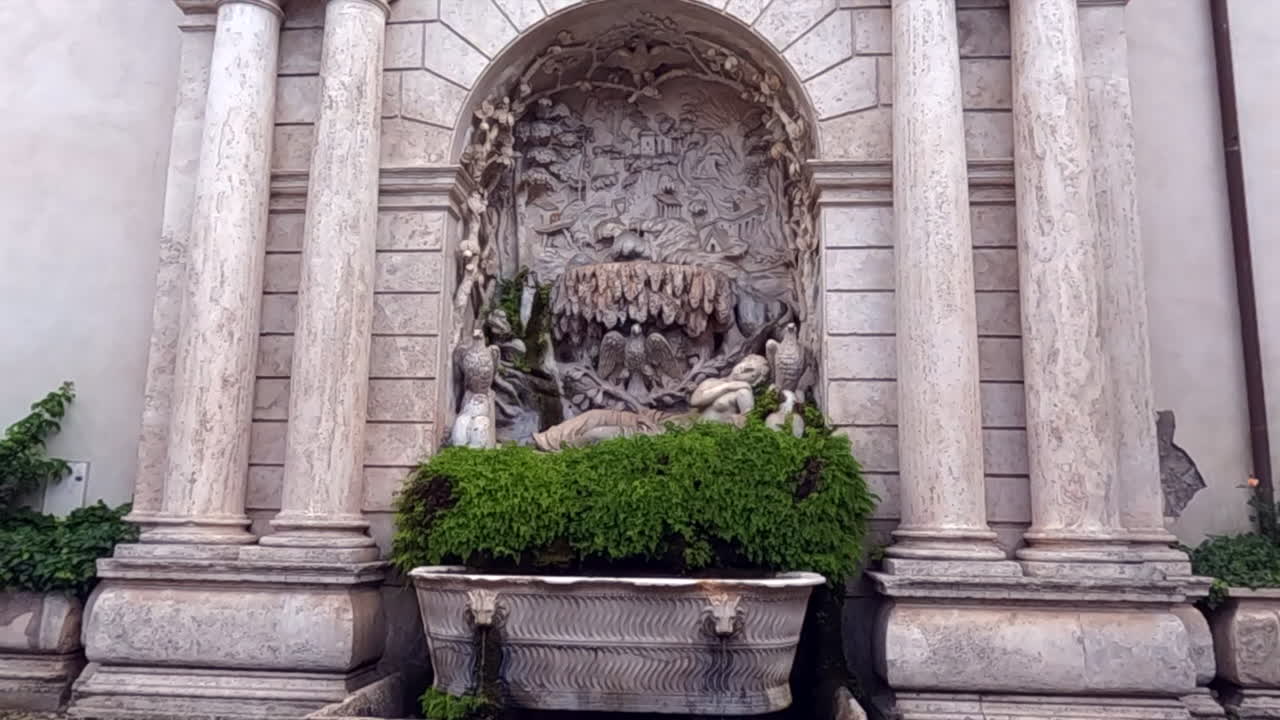 Fuente barroca de mármol ornamentada ubicada en un nicho arqueado flanqueado por columnas clásicas en Tívoli, cerca de Roma, Italia. Elegante mampostería renacentista con exuberante vegetación