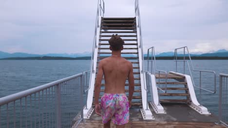 Toma-En-Cámara-Lenta-De-Un-Joven-Caminando-Hacia-El-Trampolín-Y-Subiendo-Las-Escaleras,-Observando-El-Hermoso-Paisaje-Marino