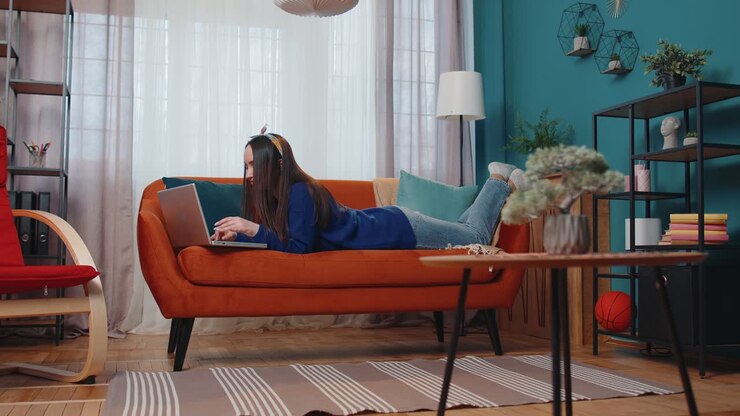 Cheerful young woman lying on sofa using laptop pc share messages on social media application
