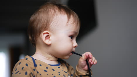 adorable caucasian kid with cute plump cheeks playing with cord. little kid shoves shoe lace into mouth. close up. blurred backdrop.