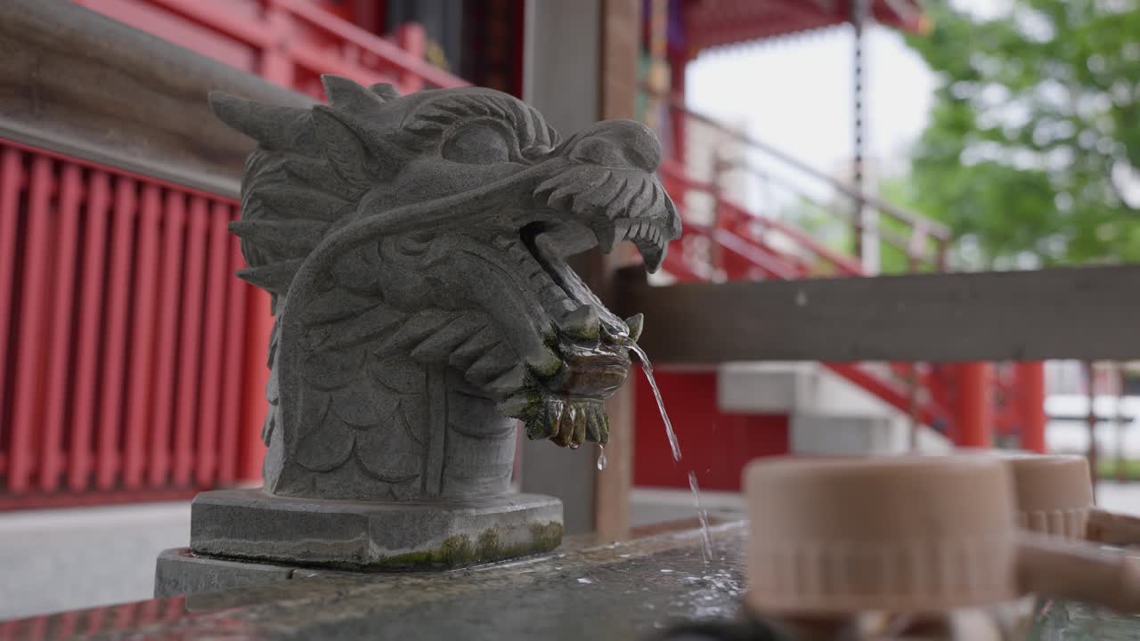 A close-up shot of a stone dragon spout with water flowing from its mouth at a traditional Japanese purification fountain