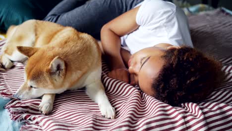 pretty african american teenage girl and her loyal dog are sleeping together on bed at home, person is hugging animal in sleep. trust and rest concept.