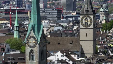 Toma-De-Paralaje-En-Movimiento-Hacia-La-Derecha-De-Las-Torres-Del-Reloj-De-Las-Antiguas-Ciudades-De-Zurich-En-Un-Clima-Soleado-Con-El-Horizonte-De-Zurich-Al-Fondo