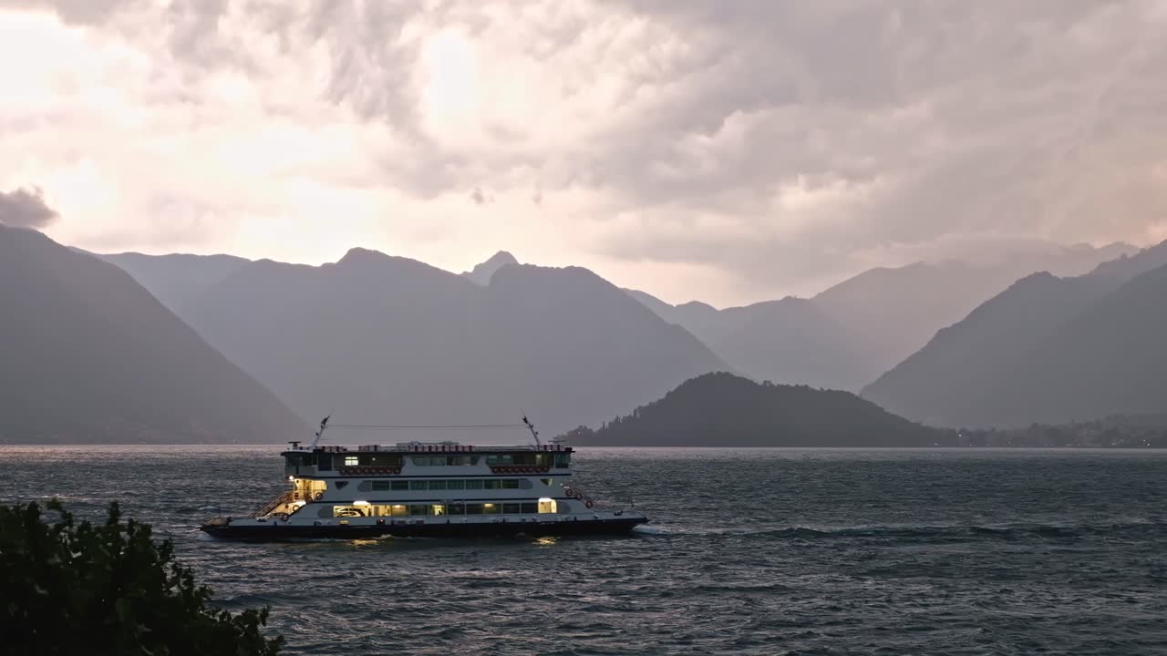 LOMBARDY, ITALY - AUGUST 02, 2018: Cinematic shot of touristic excursion boats floating on lake Como in front of the mountain at sunset
