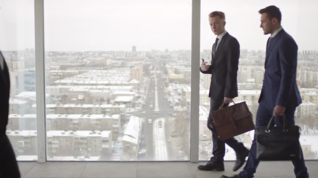бизнесмены ходят перед панорамным окном в офисном здании
