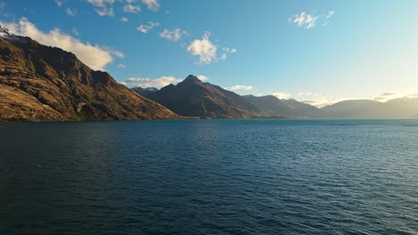 panorama de camiones aéreos a través del lago wakatipu se extiende hasta las montañas de roca de piedra arenisca roja
