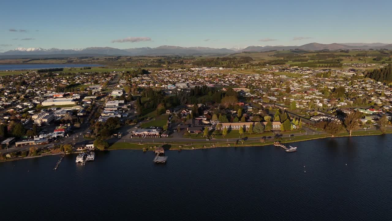 Scenic 4K aerial drone footage flying backwards from Te Anau town waterfront at sunset. Panoramic view of the settlement, Lake Te Anau, and mountains in Fiordland, New Zealand