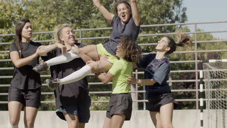 female football players raising soccer team captain after victory in competition