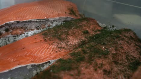 three orange trout fillets laying in box beeing sprinkled with green dill falling from above - handheld slow motion