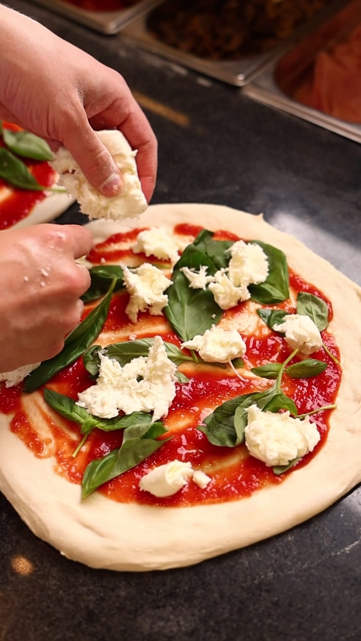 Chef che aggiunge mozzarella fresca all'impasto della pizza