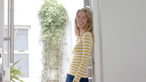 portrait of happy caucasian woman with blonde hair smiling in doorway at home, slow motion