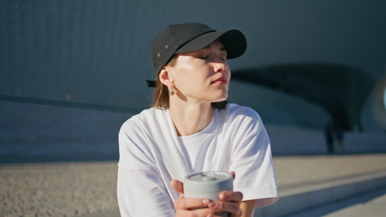 Relaxed girl holding coffee cup sitting sunny modern street closeup. Young woman