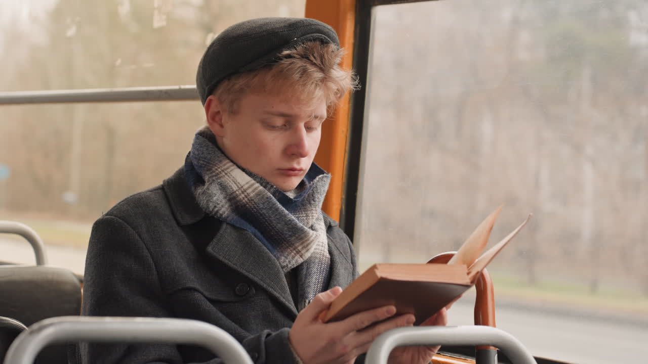Reisende Person beim Lesen. Eine Person studiert mit Schal und Baskenmütze. Konzentrierter Student, vertieft in ein Buch während des Pendelns. Schriftsteller oder Student, tief ins Lesen versunken auf einer Stadtbusfahrt.