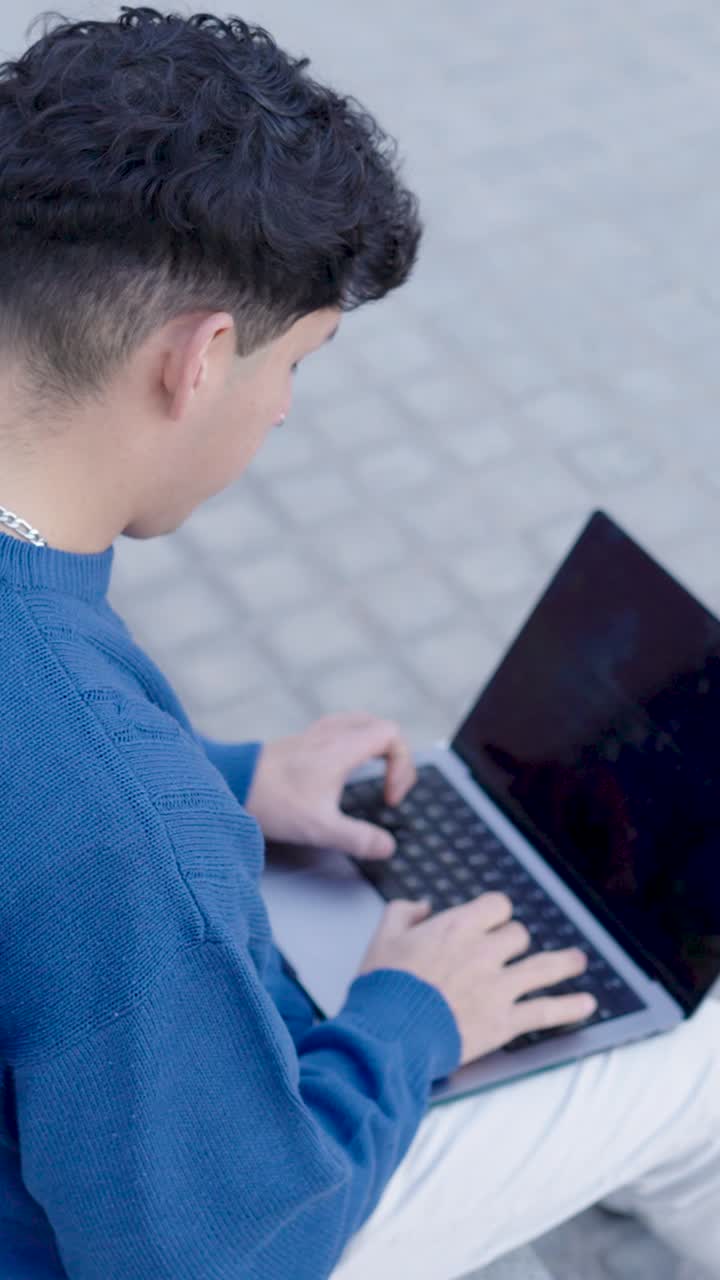 Young man typing on laptop outdoors. Vertical