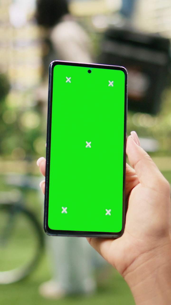 Video Verticale. Schermo verticale con chroma key su telefono cellulare tenuto contro un parco urbano sfocato.