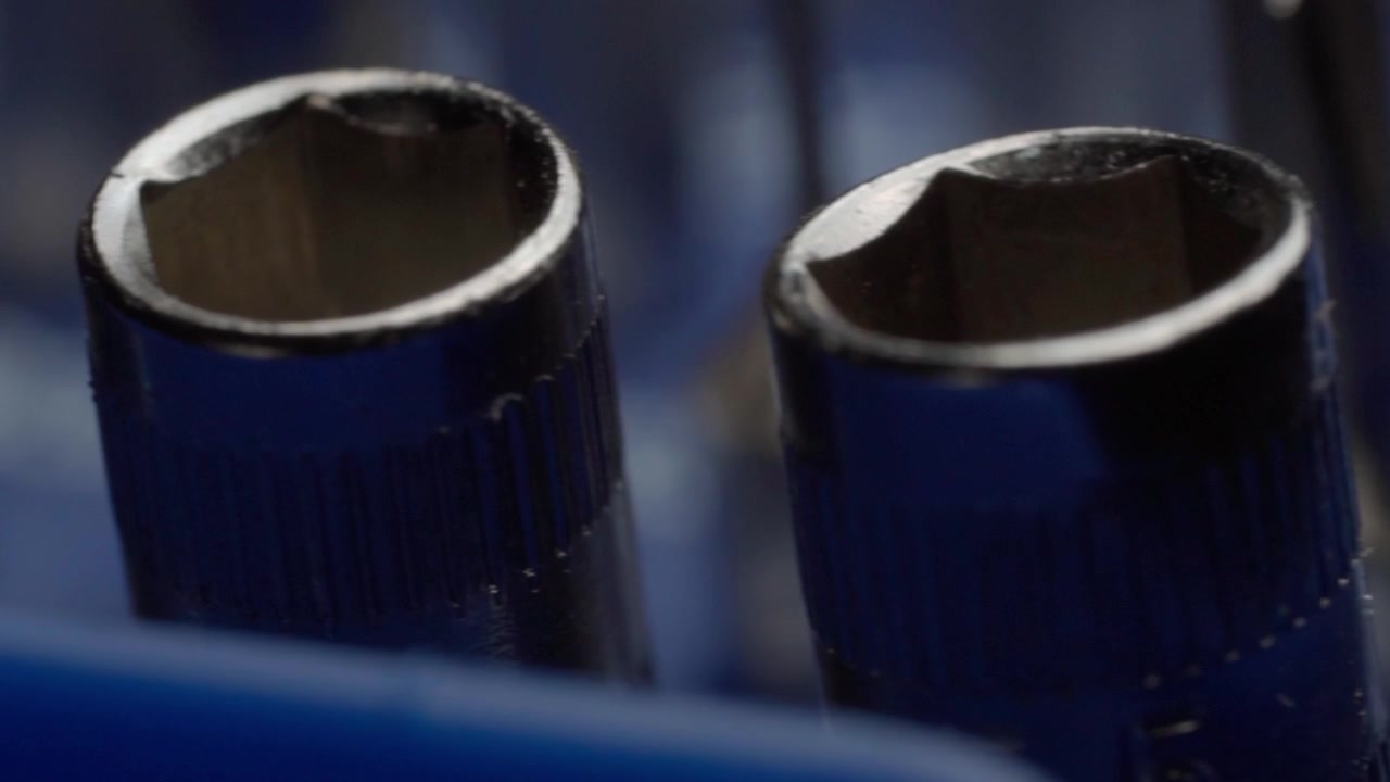 Panning close up across blue metal work tools showing hollow cylindrical ends with worn edges and industrial texture against a dark blurred background