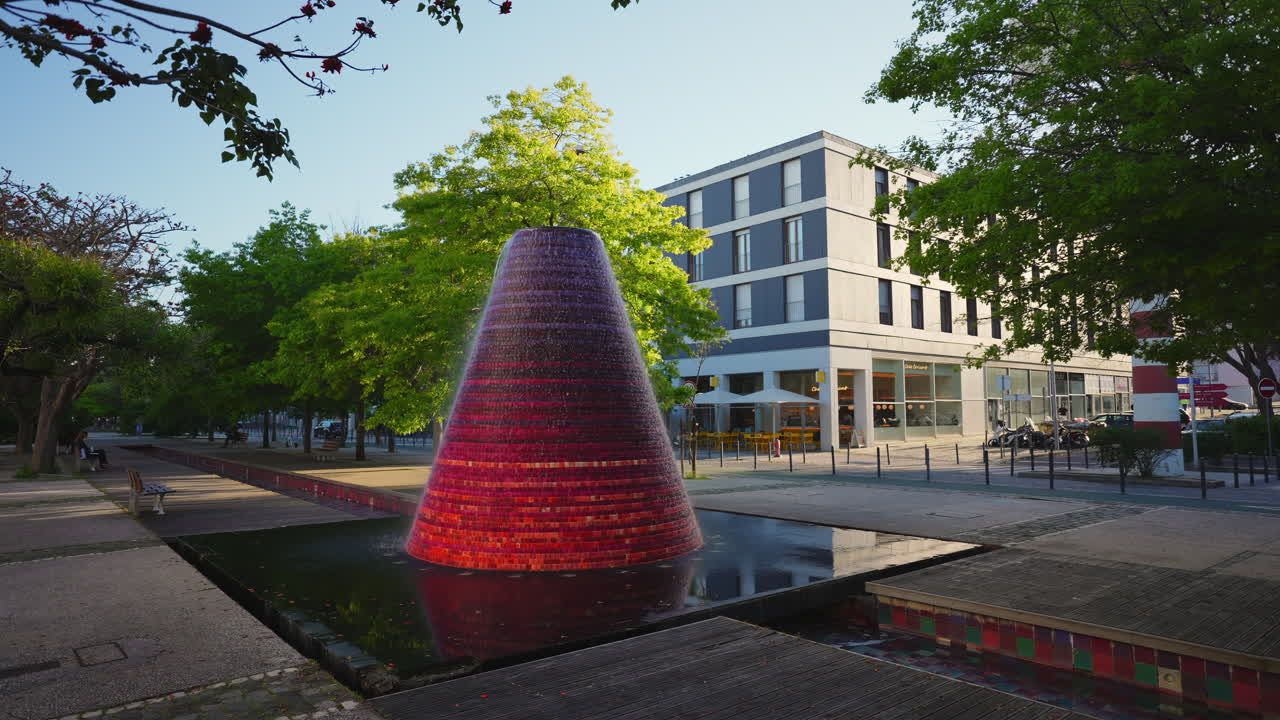 Fontana a mosaico conica in piazza cittadina con alberi al rallentatore
