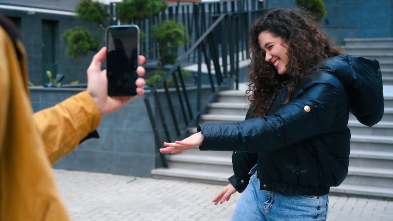 En person som filmar en ung dansande kvinnlig bloggare och influencer med en smartphone. Slow motion.