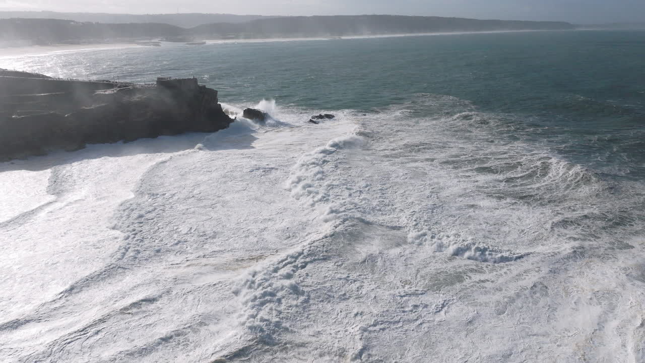 Aerial drone shot of waves coming into shore on a day with giant waves in Nazaré, Portugal, Europe. Raw Atlantic Ocean energy and power on display by the lighthouse and North Beach