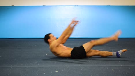 a-static-shot-of-a-guy-in-a-gymnastics-gym-doing-ab-workout-with-leg-raises-shirtless-from-a-side-front-view