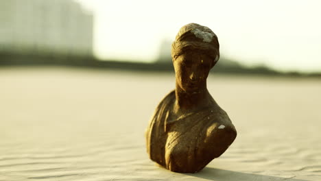 ancient sculpture stands on sandy surface at sunset highlighting lost artistry