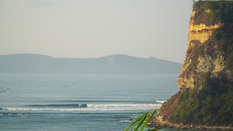 aerial static shot of gerupuk surfspot with cliffs and waves during misty day in indonesia