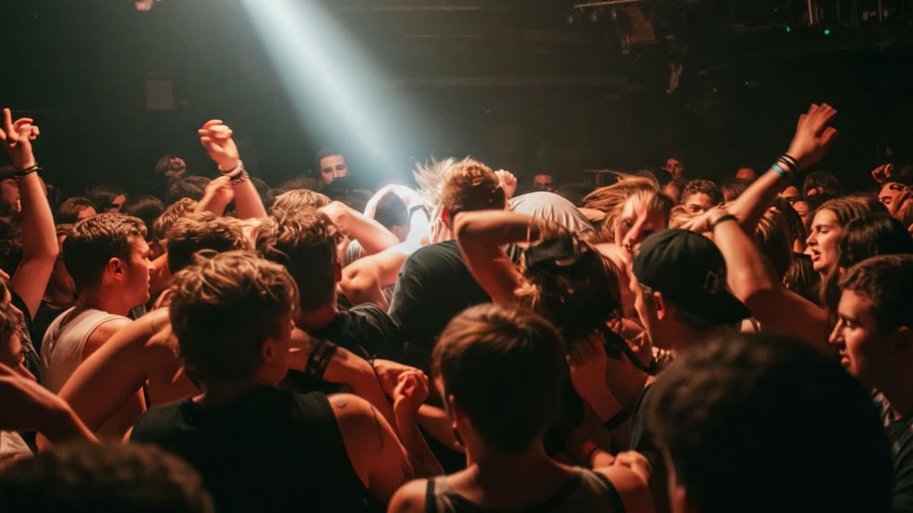 A vibrant crowd experiencing an electric atmosphere at a live music performance, illuminated by a single beam of light cutting through the energetic sea of attendees