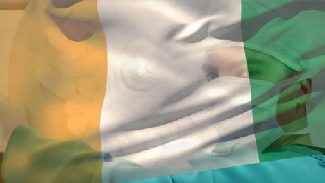 animation of flag of ivory coast over biracial male surgeon with face mask