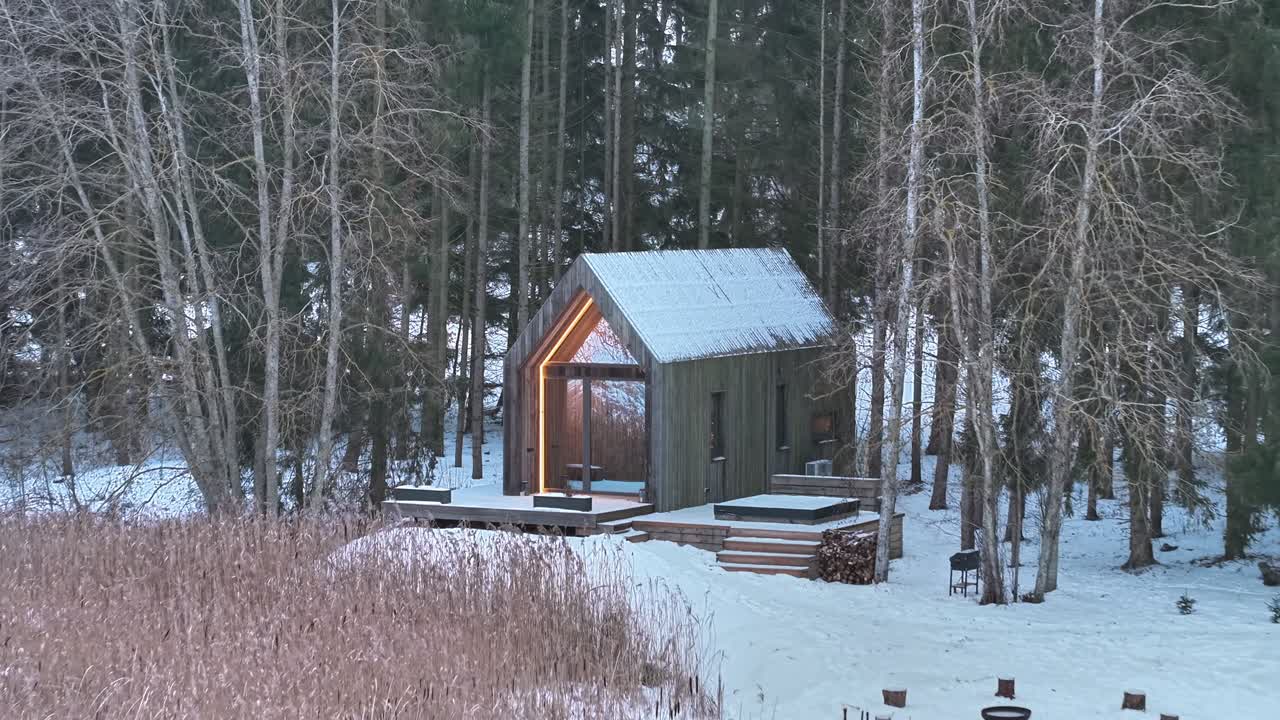 Volo con drone all'indietro da un moderno campeggio con cabine in legno in un ambiente di foresta innevata, Tervete, Lettonia.