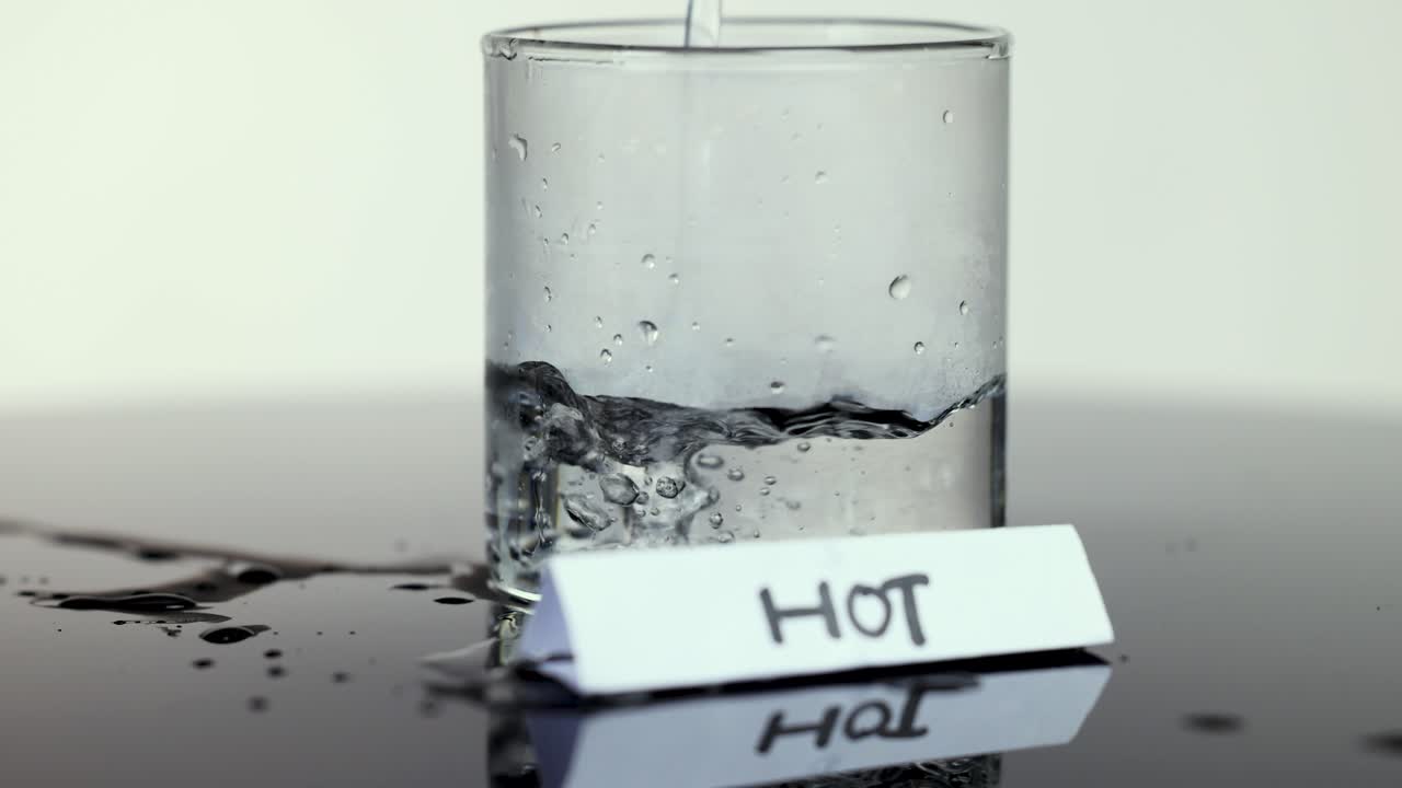 Hot water poured into clear glass, creating bubbles and steam, under bright, even studio lighting