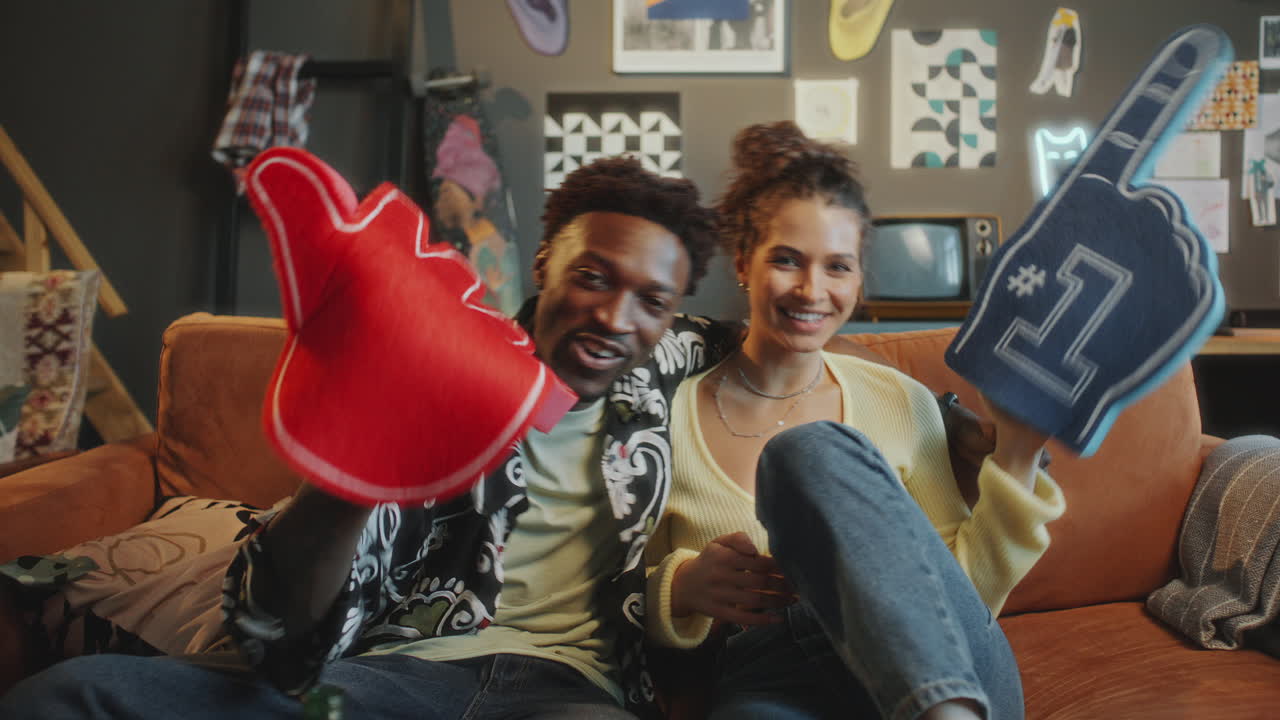 Excited Couple Cheering with Foam Fingers while Watching Sports Game at Home