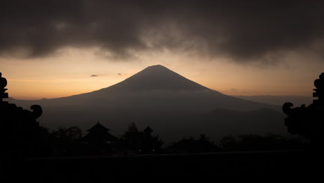 Mount-Agung-Vulkan-Während-Des-Sonnenuntergangs-Zur-Goldenen-Stunde-Mit-Sich-Schnell-Bewegenden-Dunklen-Wolken-Und-Tempelstrukturen-Im-Vordergrund