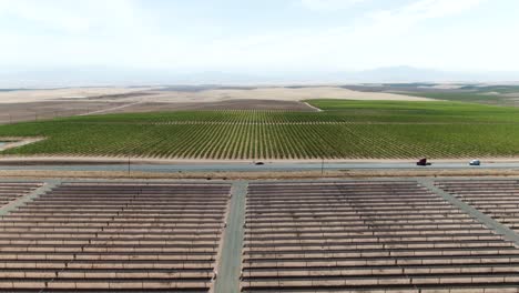 High-altitude-forward-moving-aerial-over-a-field-of-solar-panels-overlooking-vineyards-far-ahead-and-a-country-road-dividing-both