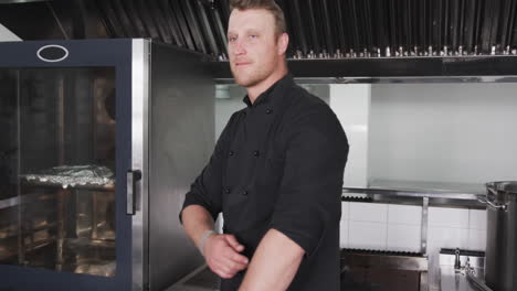 portrait of happy caucasian male chef in black smiling in kitchen, slow motion