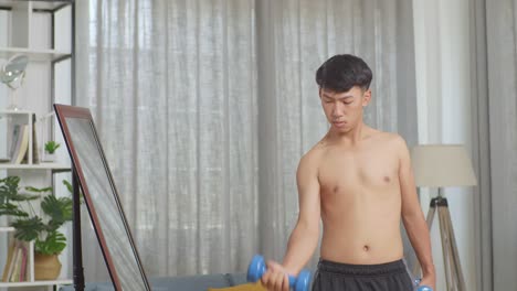 asian teenager boy training with dumbbells while doing shirtless workout at home