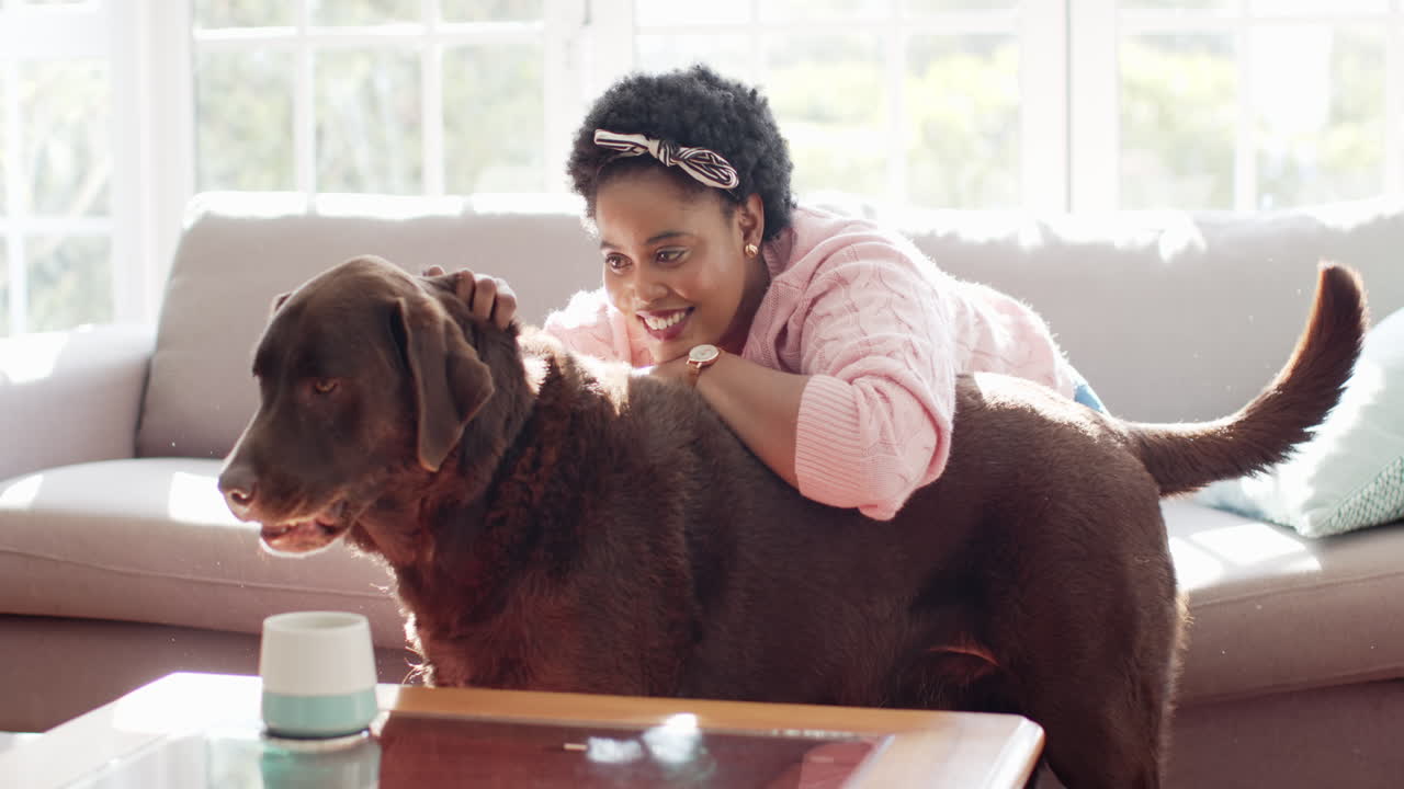 una mujer afroamericana abraza a un gran perro labrador marrón en el interior de su casa
