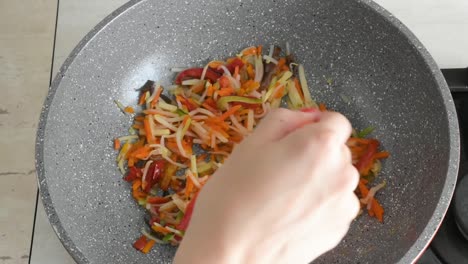 woman's hand stirring chopped vegetables frying in a wok