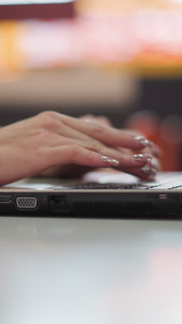 elegante primer plano de manos femeninas escribiendo en una computadora portátil, mostrando uñas pintadas y un entorno de trabajo profesional con luces borrosas en el fondo