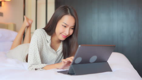 in a work from anywhere lifestyle, a pretty young businesswoman opts for working on her digital tablet while laying on her hotel bed