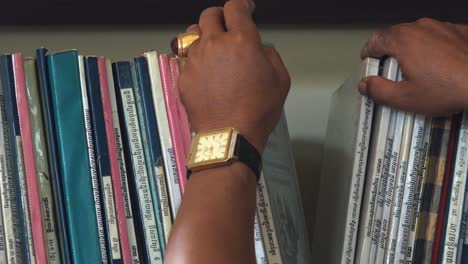 Close-Interior-Shot-of-Hand-of-Man-Searching-for-Books-on-Shelf-in-the-Day