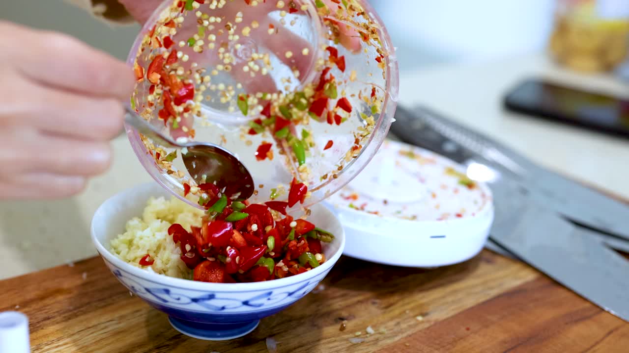 Hands mixing chopped chili and garlic in a bowl on a wooden board under bright lighting