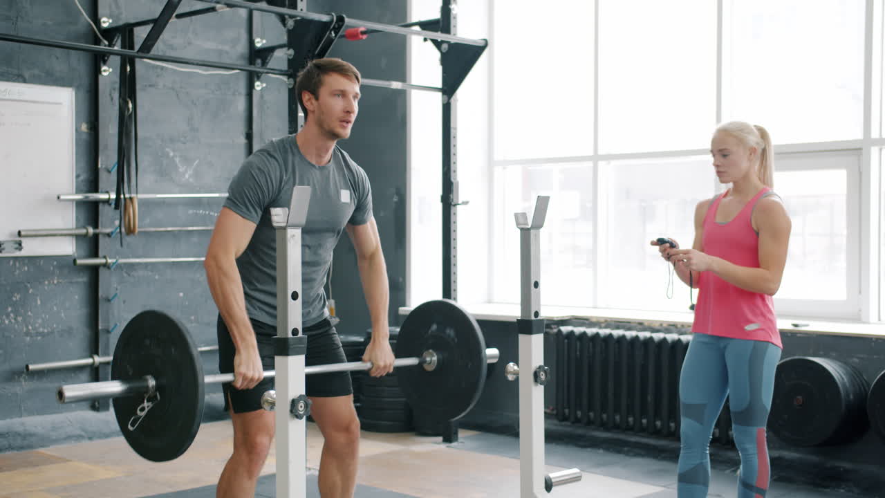 Man lifting barbell with trainer watching