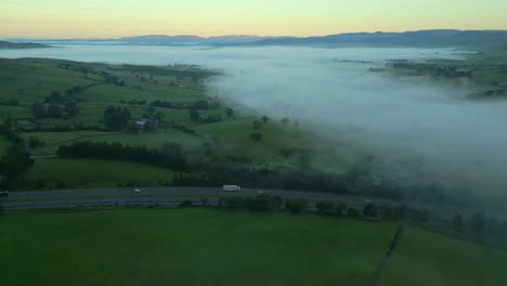 m6 motorway, green patchwork fields, fog bank and distant mountains at dawn