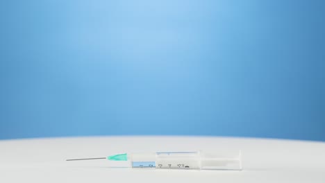 guantes azules mano coloca jeringa médica con vacunación hacia abajo, fondo azul
