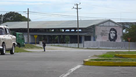 un automóvil conduce por una carretera cerca de un edificio decorado con la pintura revolucionaria del che en la cuba comunista 1