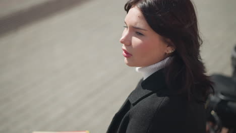 close-up of woman turning her head to the side, brown hair flowing with movement, eyes focused ahead, background features a blurred object near her